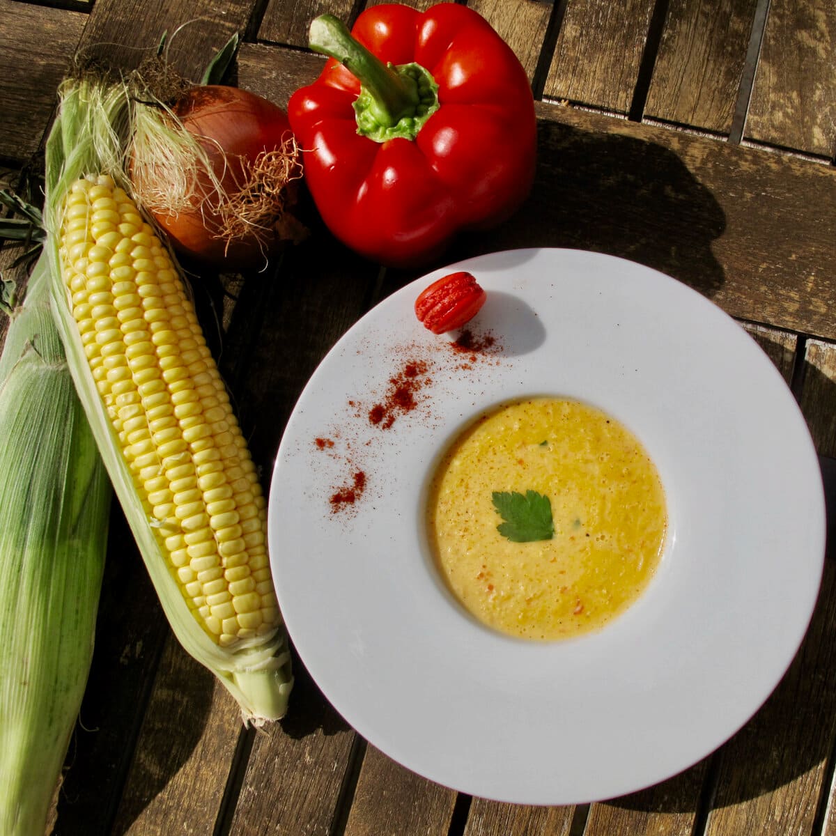 large white bowl of corn chowder with a mini red macaron, red pepper and fresh corn