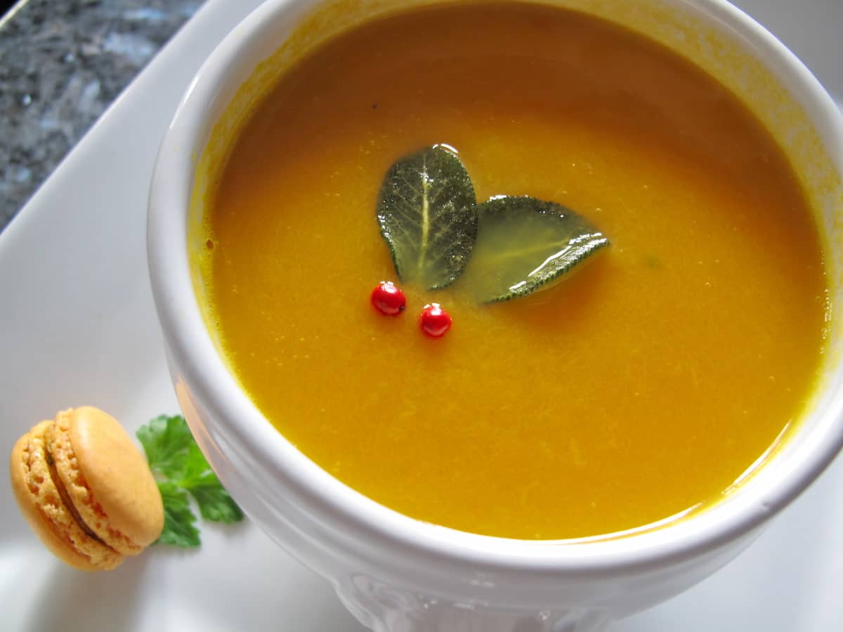 French lion bowl of pumpkin soup garnished with sage holly and a mini macaron