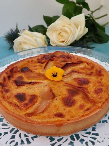 Round toasted custard tart with apples topped with an edible flower