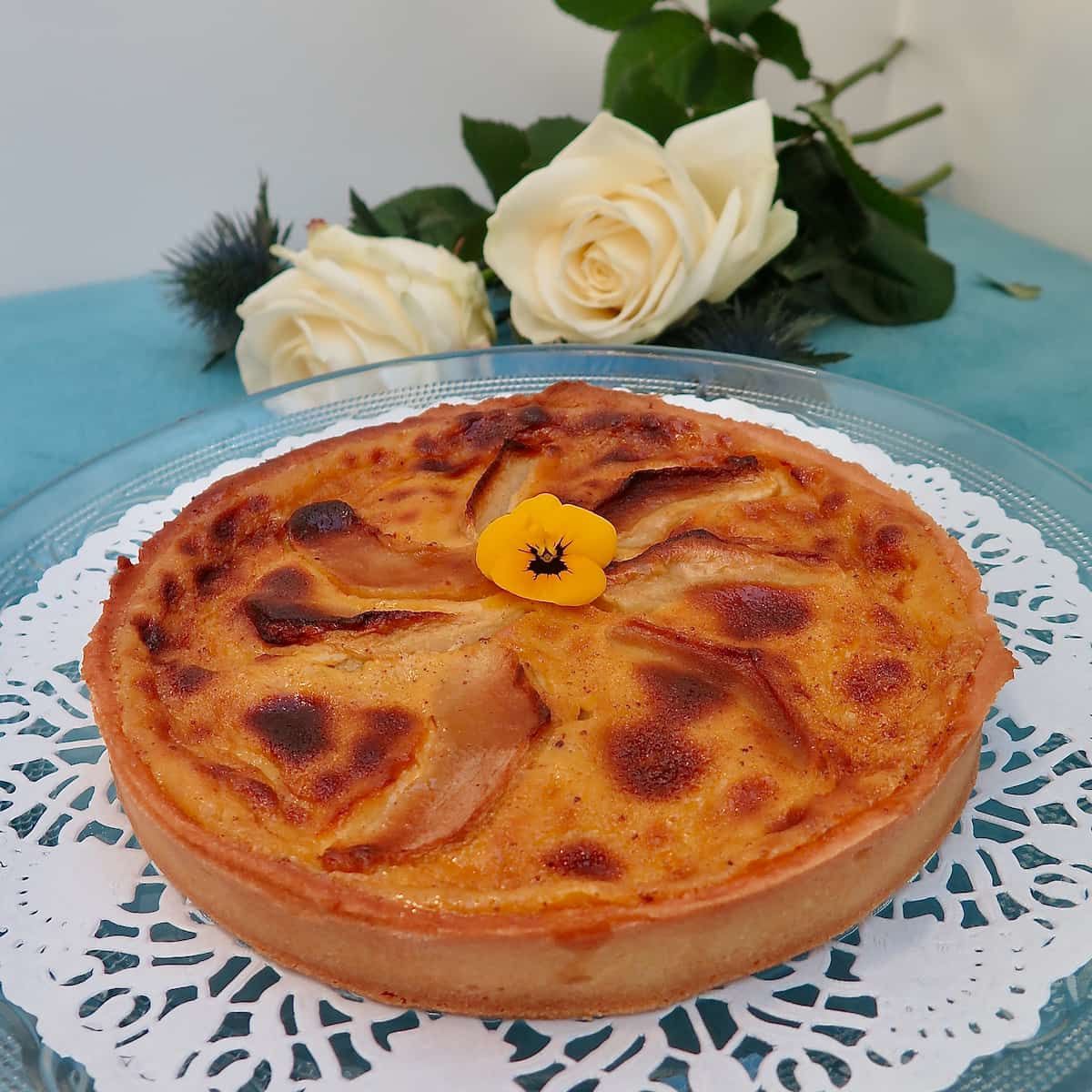 Round toasted custard tart with apples topped with an edible flower
