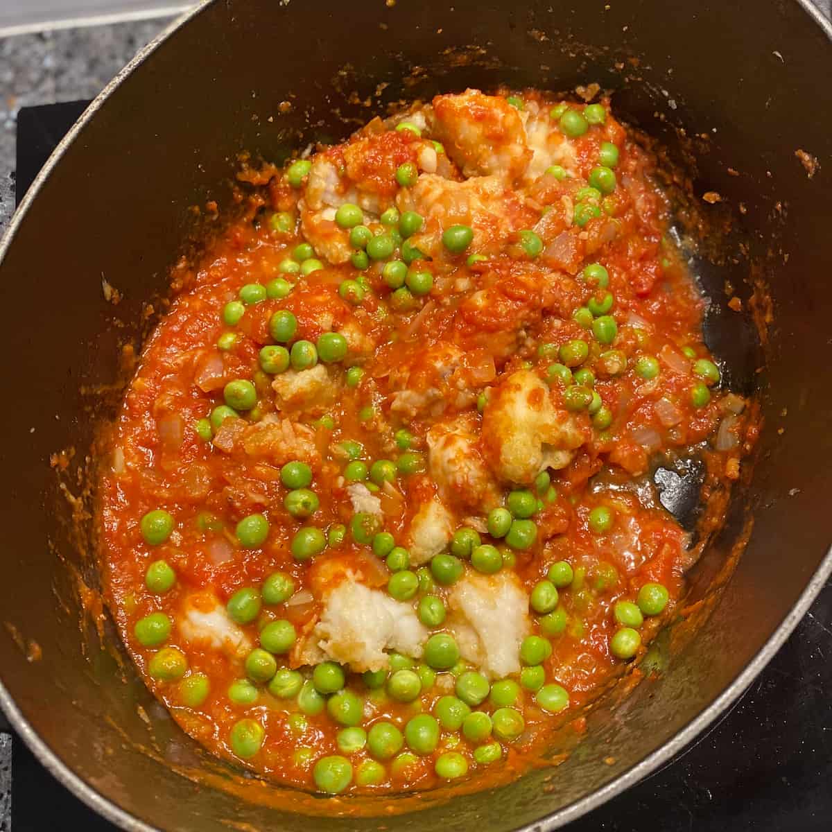 fish tomato stew in pot with fresh peas
