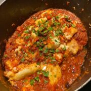 black pot with bubbling tomato and fish stew topped with chopped parsley