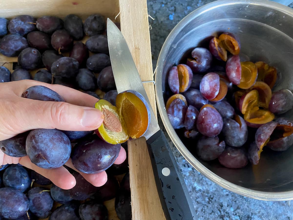 cutting purple plums in half to remove stones