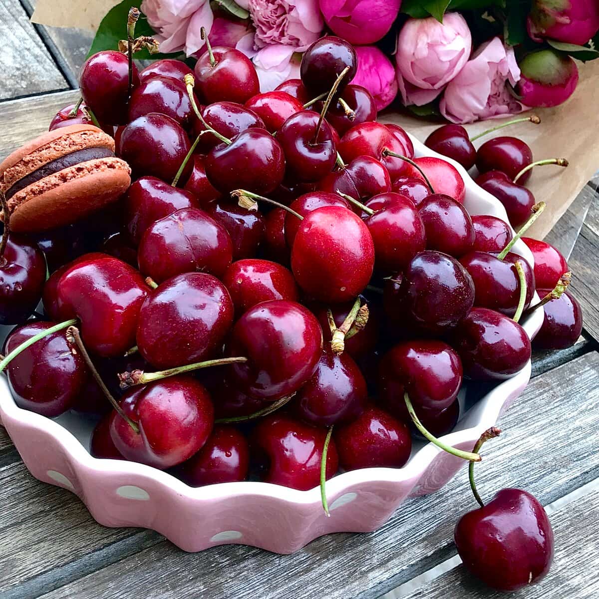 bowl of dark cherries with peonies and a chocolate macaron