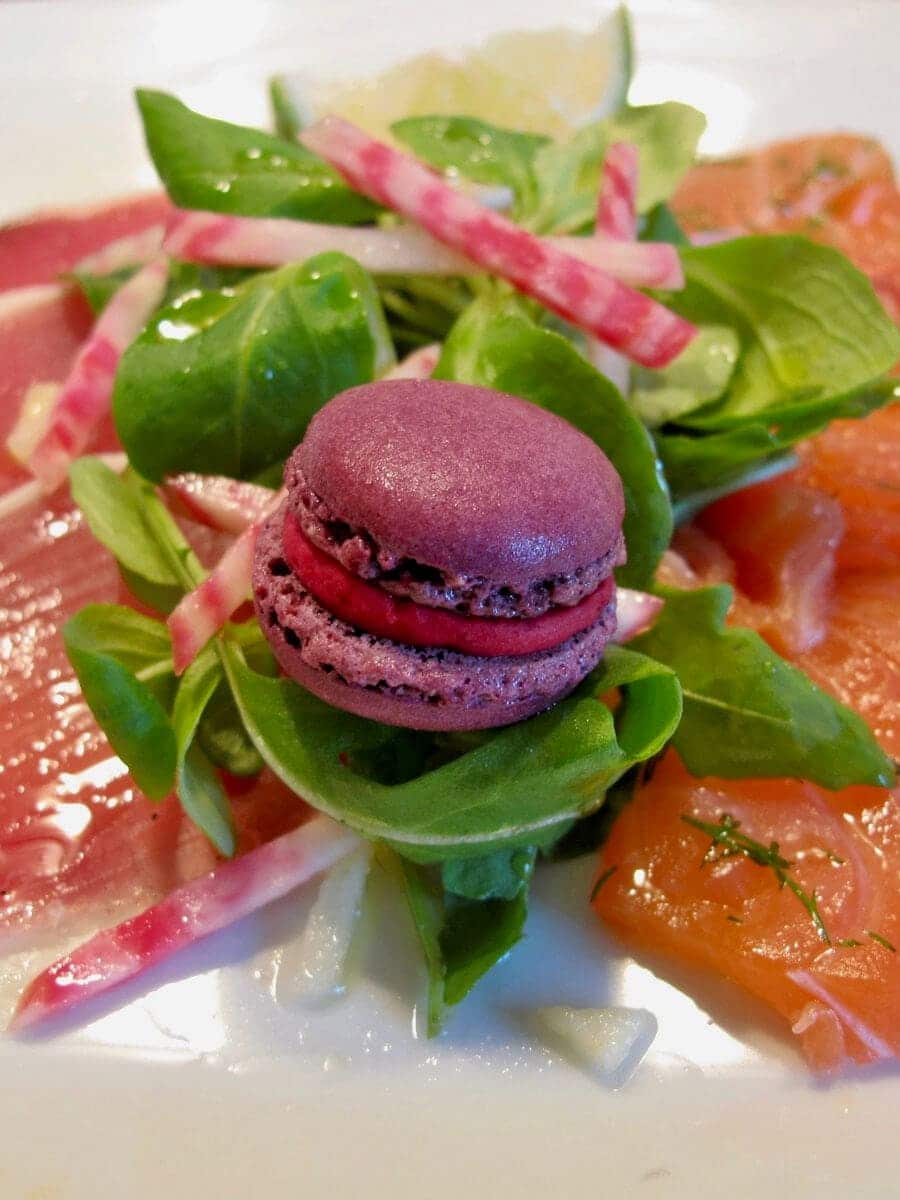 charcuterie (cured hams) with smoked salmon and salad on a plate, topped with a purple savoury macaron