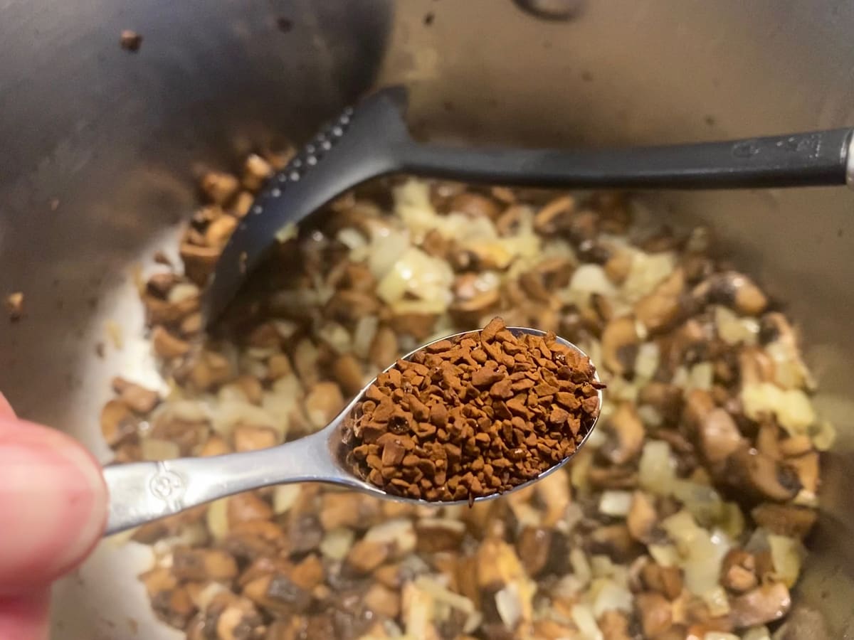spoon of coffee granules in front of a pot of cooked mushrooms