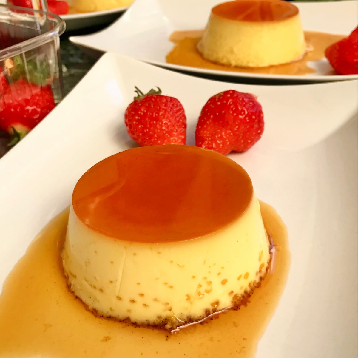 creme caramel on white plate with sauce and strawberries
