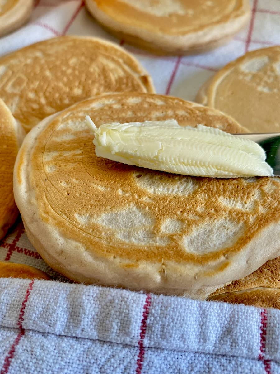 small golden brown thick pancakes with knife spreading butter as they're wrapped in a teatowel