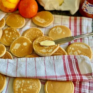 golden little thick pancakes in a tea towel with one being spread with butter