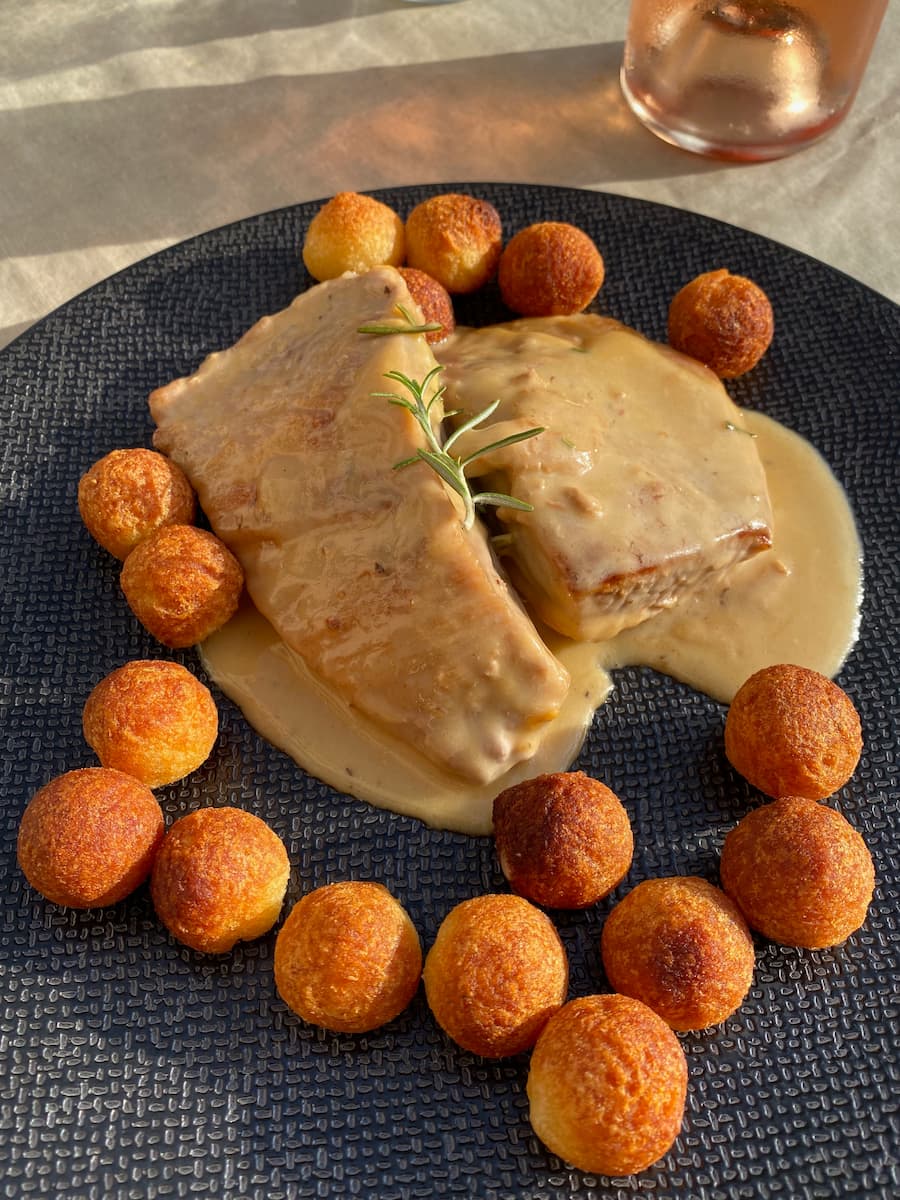Pork with rosemary sprig, topped with creamy sauce and surrounding by crispy potatoes