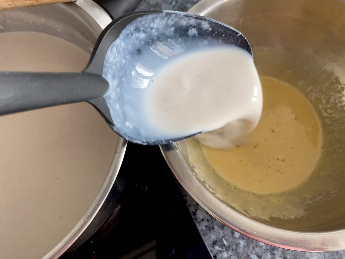 spooning hot rice pudding milk into yolk mixture