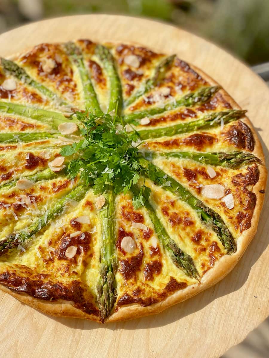 round tart on wooden board with asparagus spears laid out like the rays of the sun
