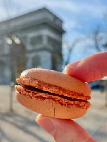 holding a macaron with ruffled foot in the shells in front of the Arc de Triomphe in Paris