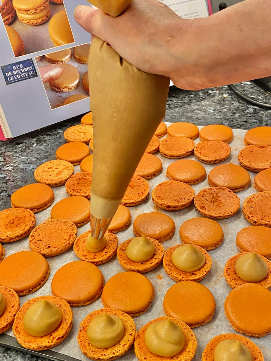 piping out a caramel cream filling on to macaron shells