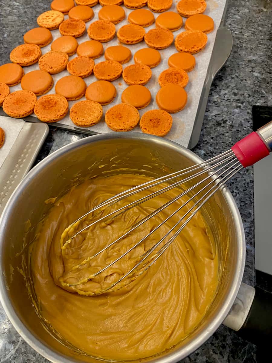 whisking together a caramel mixture with macaron shells in the background