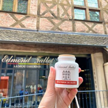 holding a ceramic pot of mustard in front of a historical timbered shop