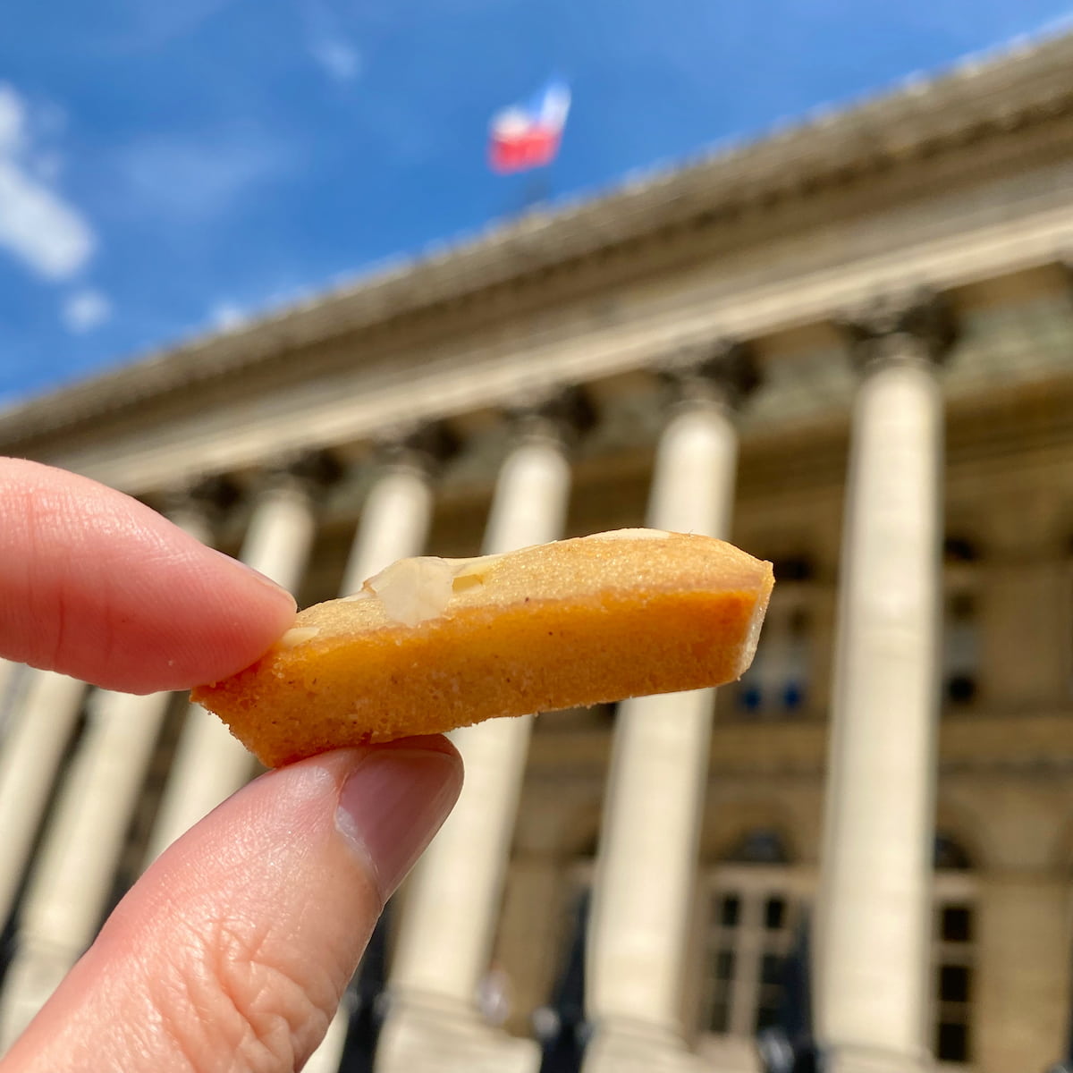 holding a golden bar shaped cake in front of the Paris Bourse