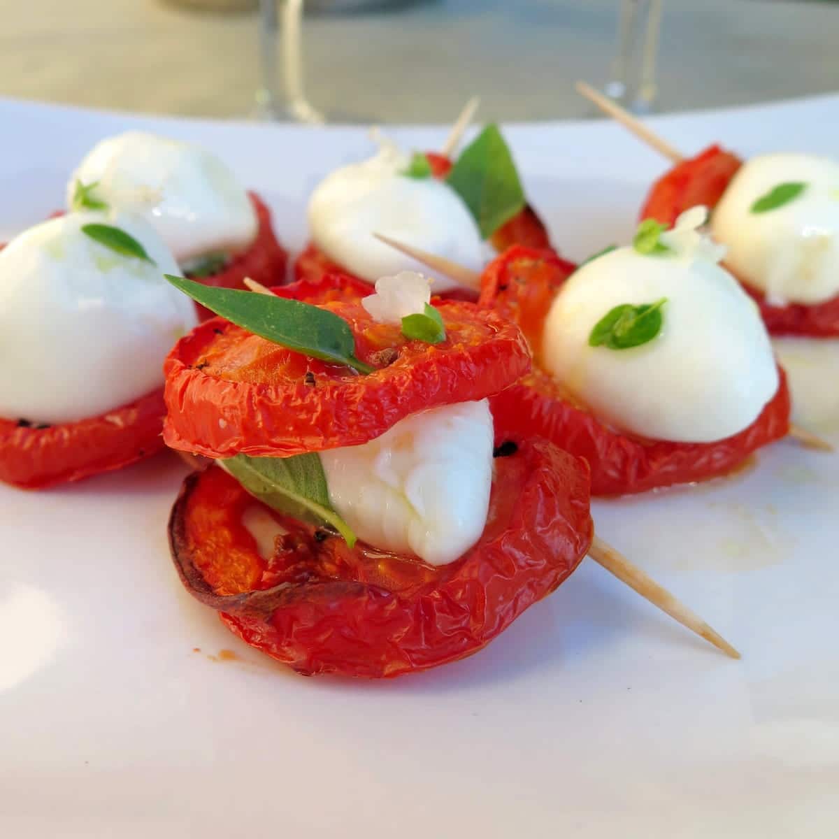 slices of roasted tomato with mozzarella cheese and basil held together with cocktail sticks