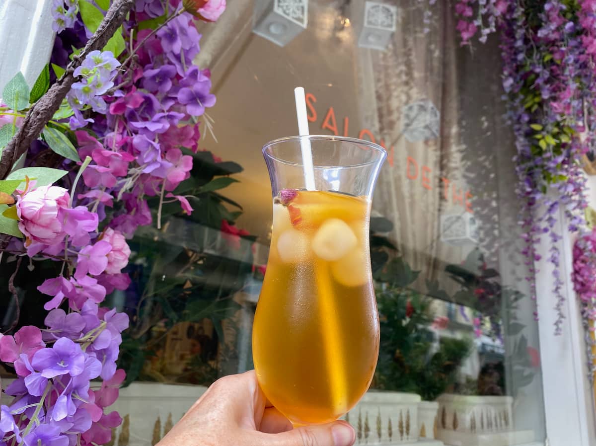 holding large glass of iced tea in front of fake flowers at a Parisian cafe