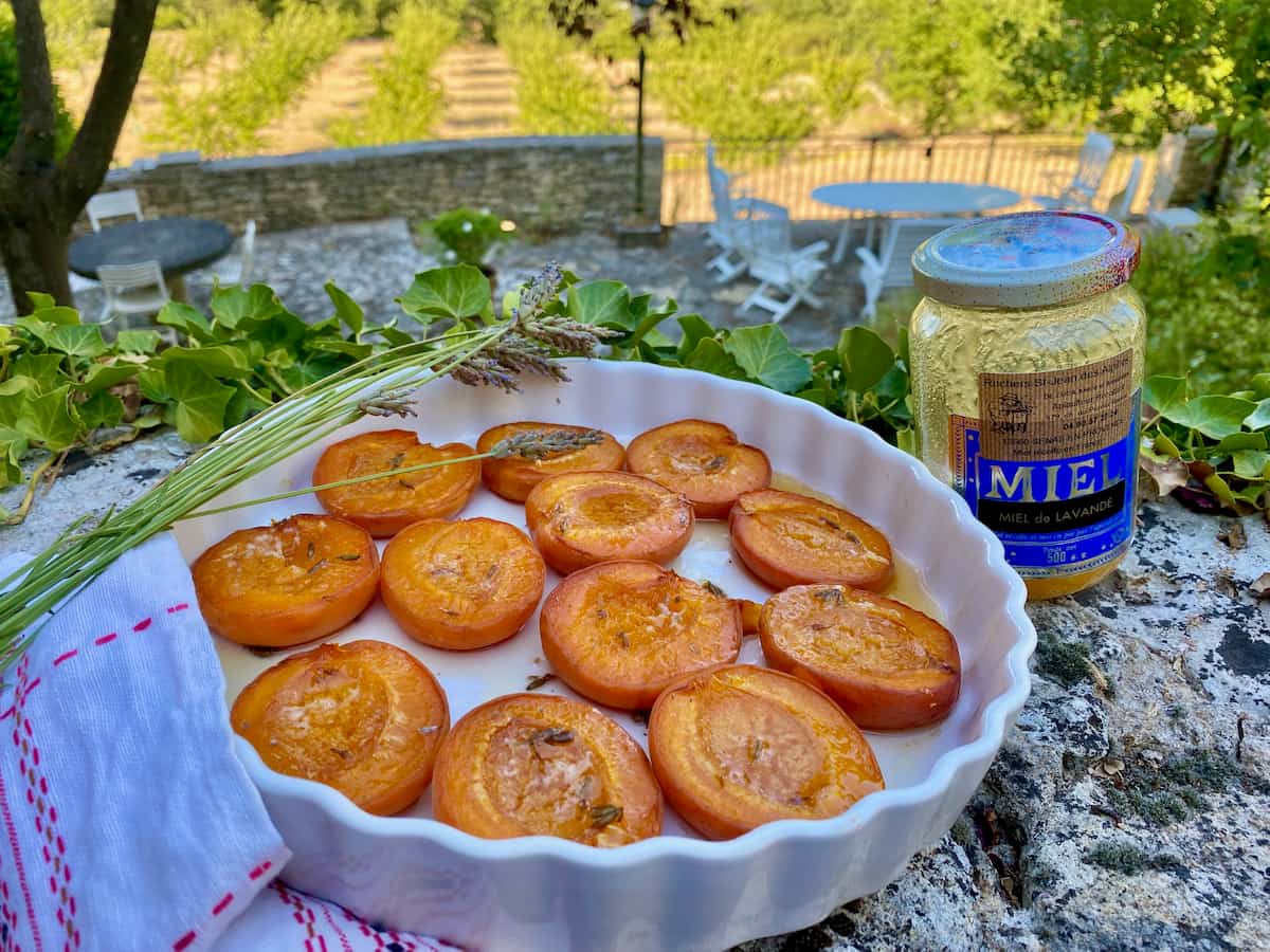 baking dish with roasted apricots halved on a stone wall with lavender and pot of French honey