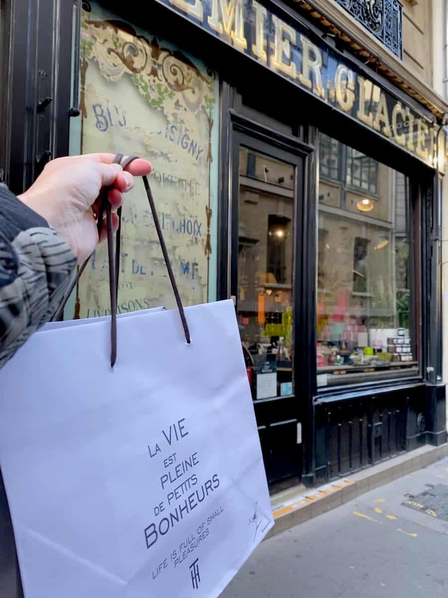 holding a French bag in front of an antique shopfront in Paris