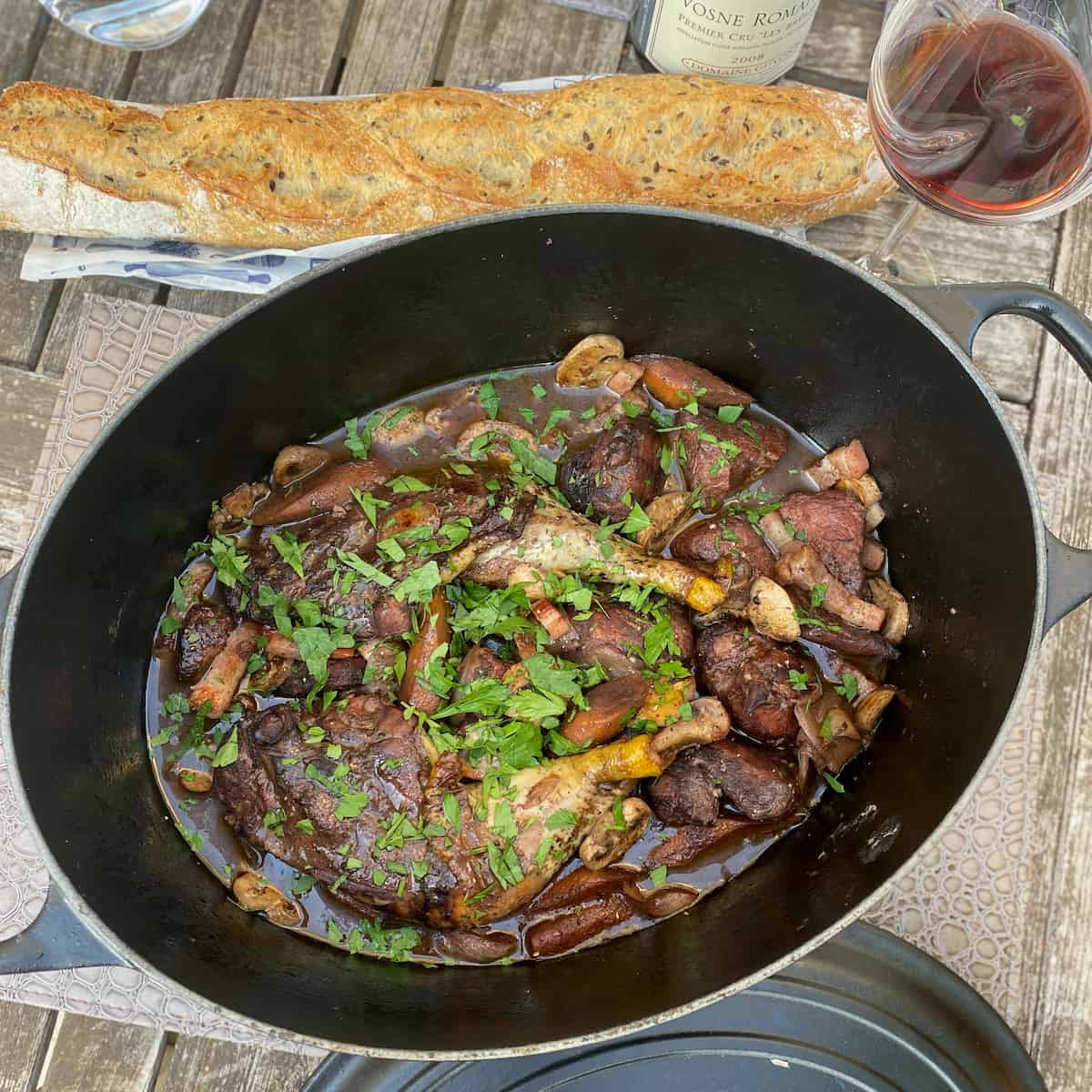 oval dish with chicken in red wine and vegetables with a French baguette