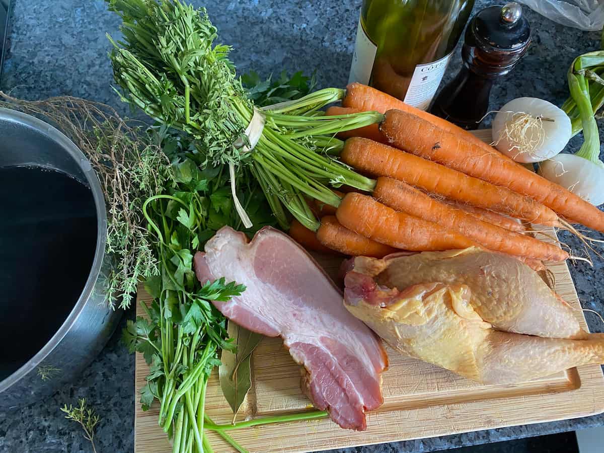 bunch of carrots, bacon, chicken, herbs, bacon, wine on chopping board