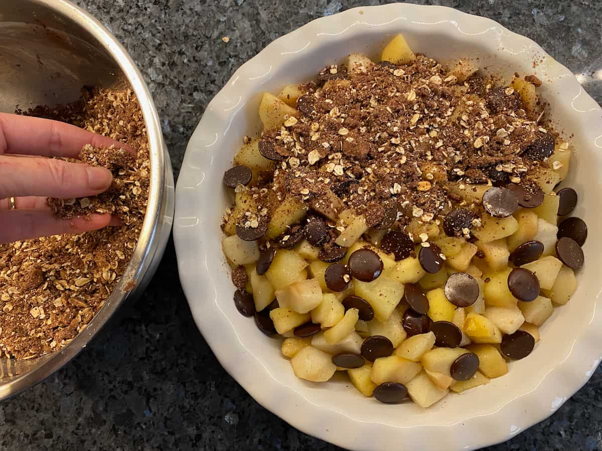 sprinkling on chocolate crumble on to cooked diced pears and apples topped with chocolate buttons