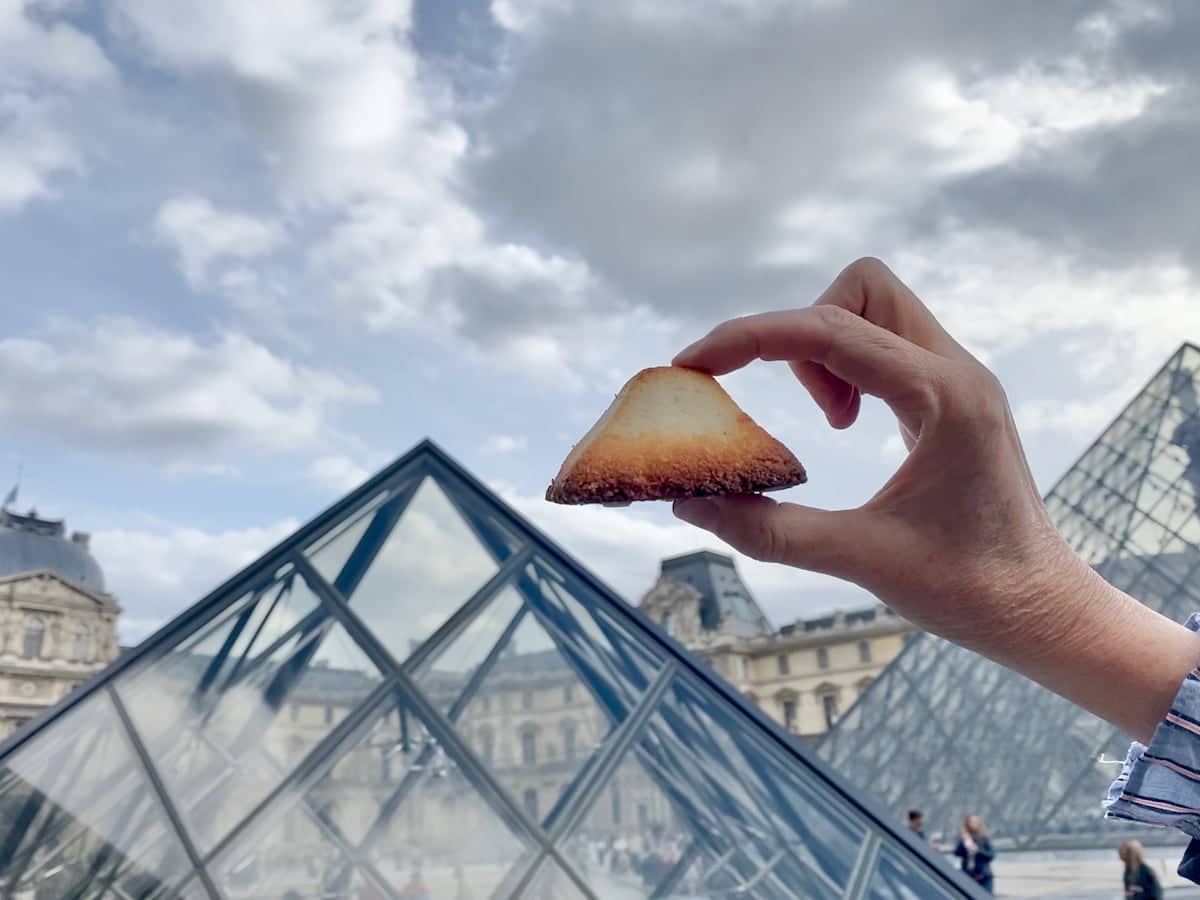 holding a pyramid shaped cookie next to the Louvre glass pyramid in Paris