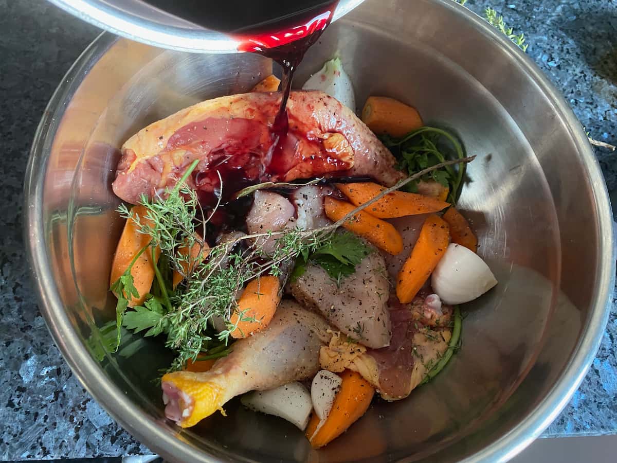 pouring red wine onto poultry, vegetables and herbs