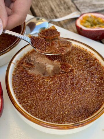cracking in to a milk chocolate crème brûlée showing a delicious set custard topped with a thin caramelised crust - served with halved passionfruits