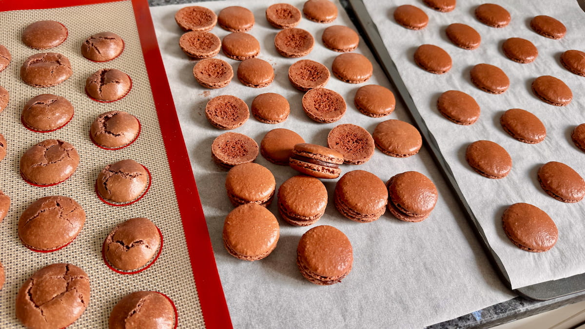perfect chocolate macaron shells baked on parchment paper and cracked shells with no feet on a silicone mat