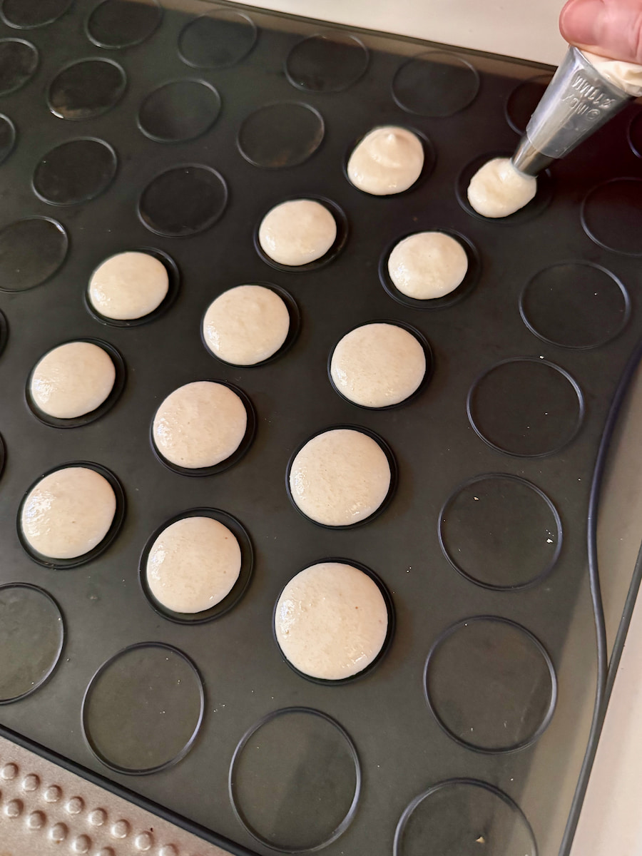 piping macaron batter into the middle of a raised macaron mat, trying to aim for the centre