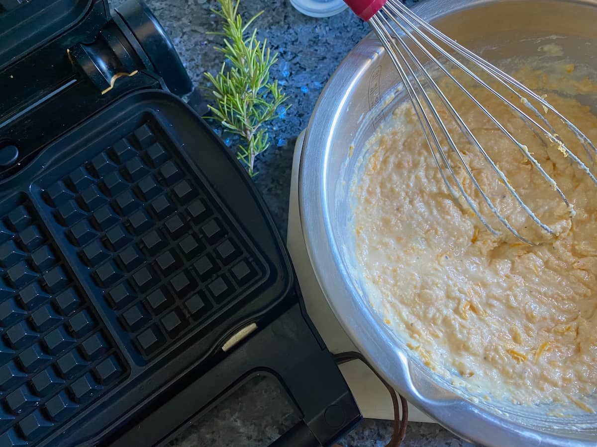 whisking a cheese batter next to a waffle iron