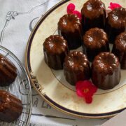 plate of dark caramelised cannelés de Bordeaux with red edible Begonia flowers