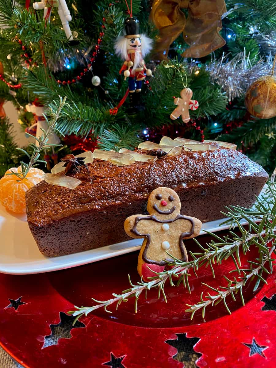 loaf of glossy gingerbread topped with candied ginger with a decorated gingerbread man