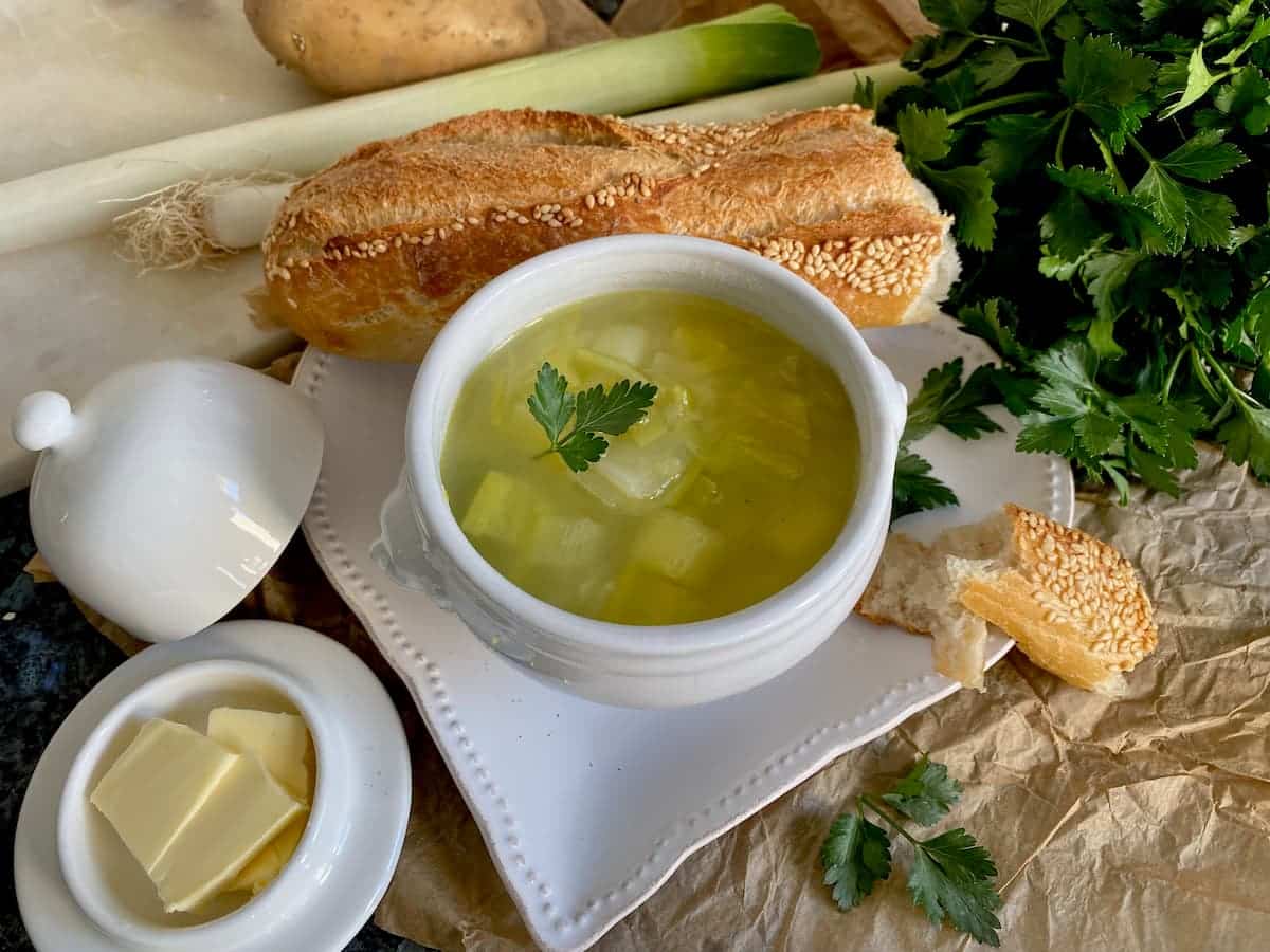 porcelain bowl of leek and potato soup with French bread and butter