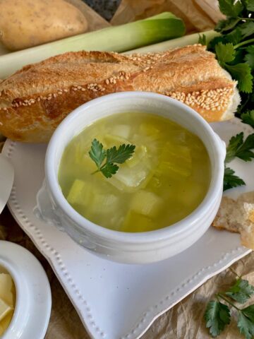 French white porcelain bowl of leek and potato soup with a baguette and butter