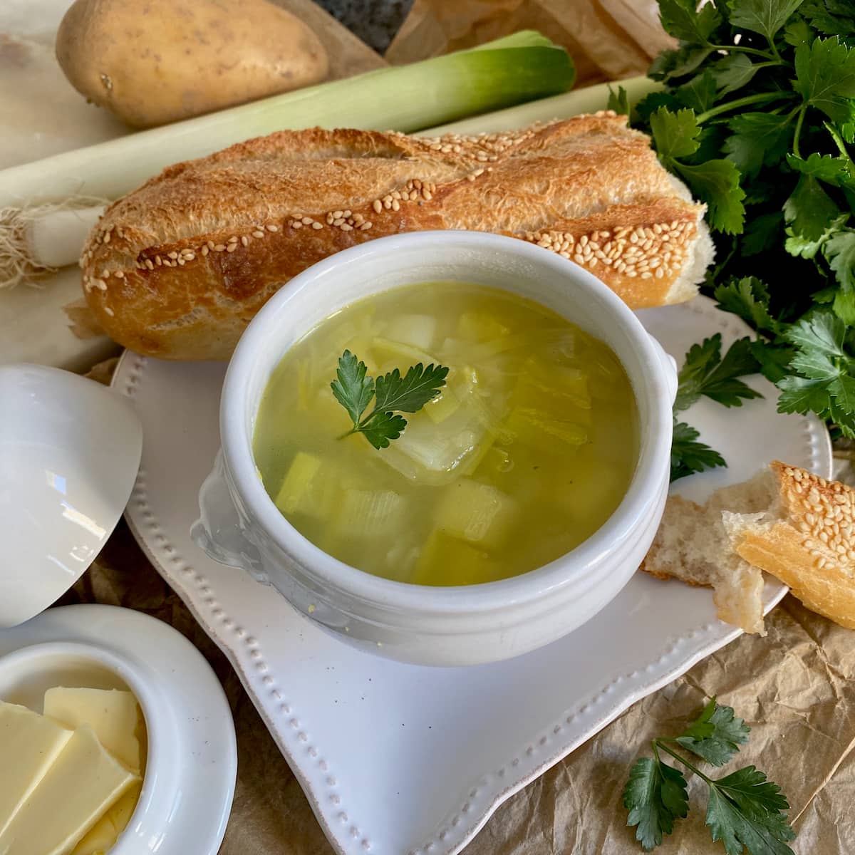 French white porcelain bowl of leek and potato soup with a baguette and butter