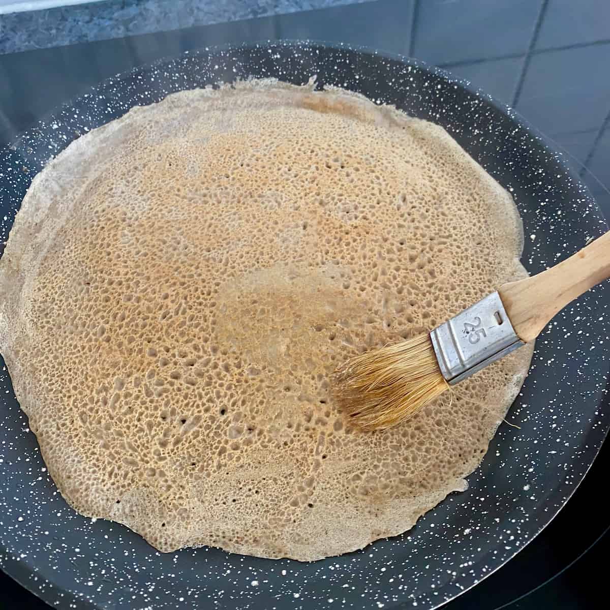 brushing melted butter on to a thin pancake in a pan