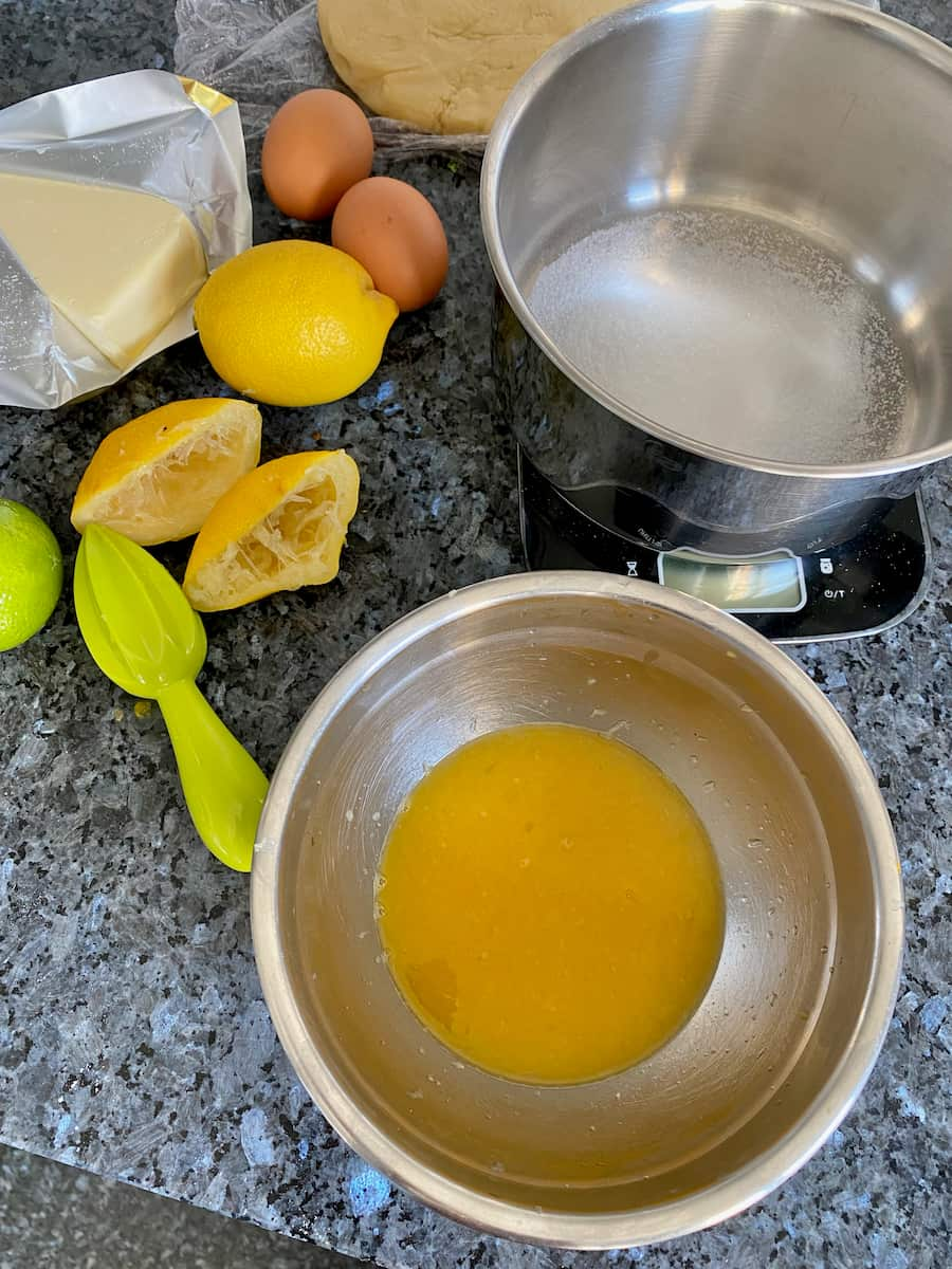 bowl filled with lemon juice, squeezed lemons, eggs and another bowl of sugar on digital scales