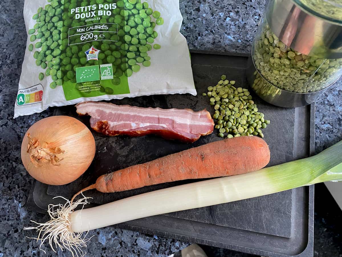 ingredients laid out for soup: onion, dirty carrot, leek, bacon and either split peas or fresh/frozen peas