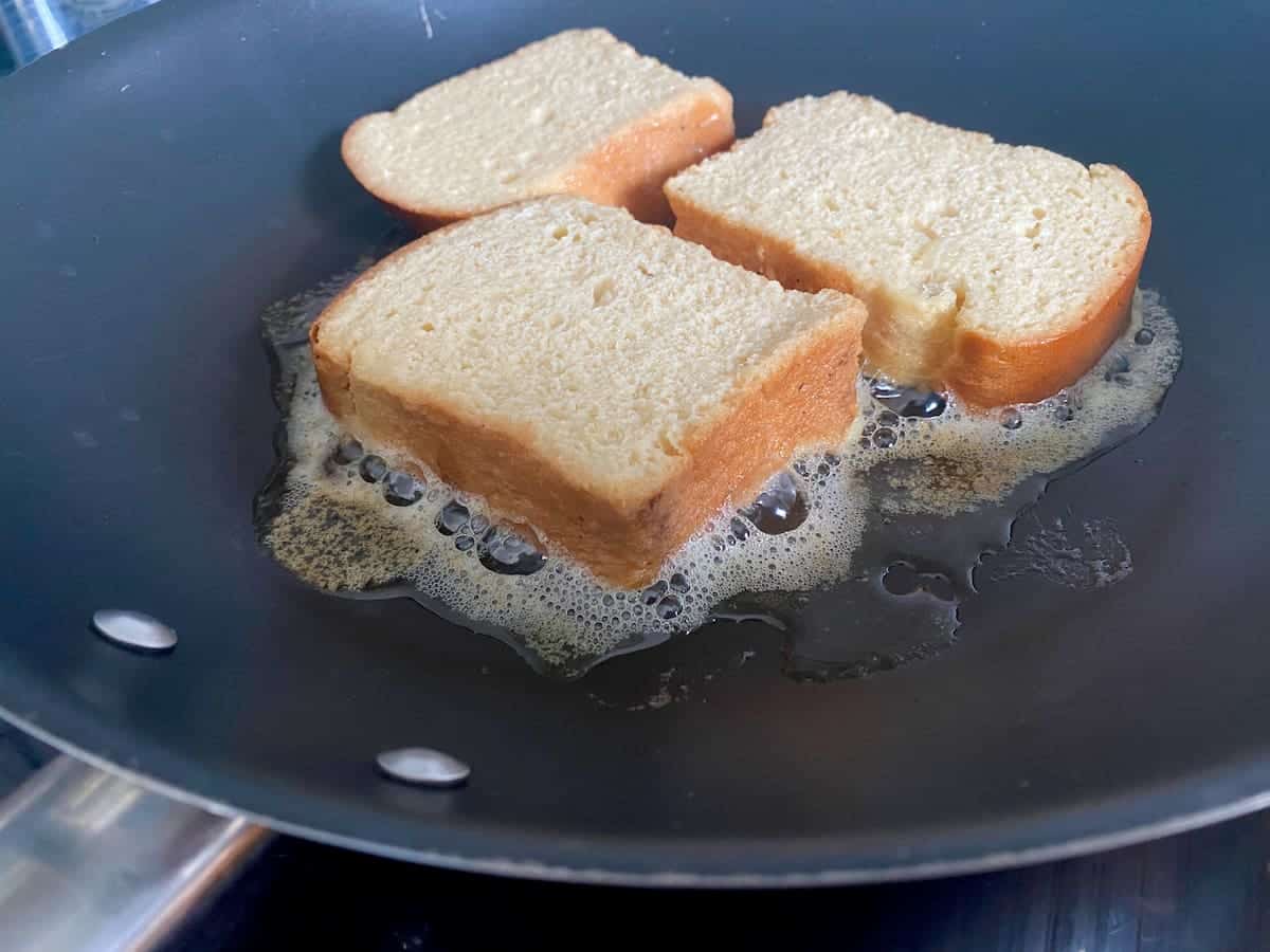 three slices of eggy bread in a frying pan sitting on top of foaming butter