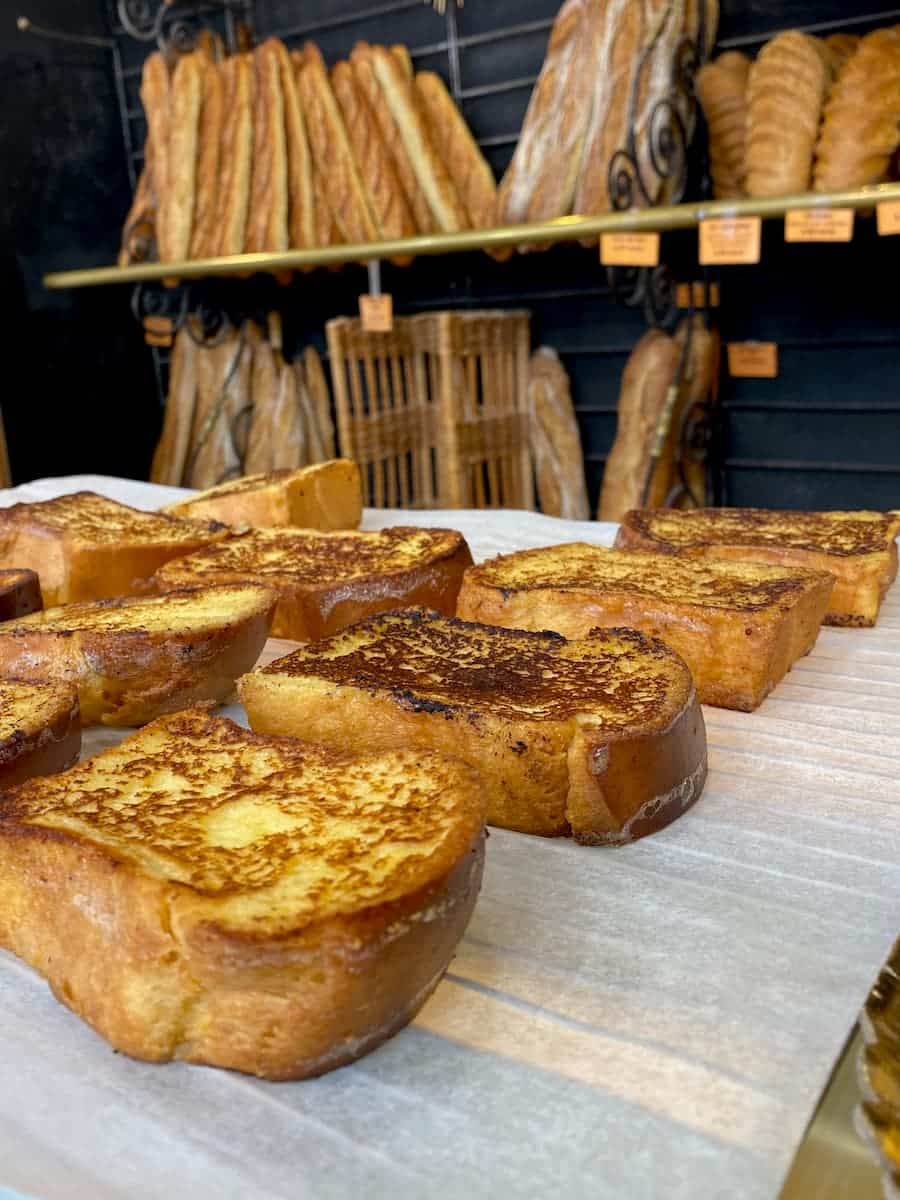 tray of the best French toast recipe for golden brown eggy bread in a French bakery in front of baguettes and loaves