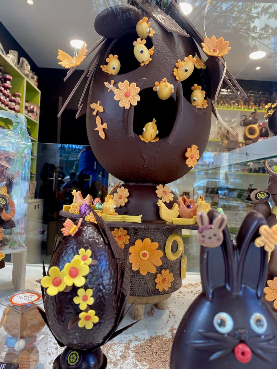 giant easter chocolate egg with yellow and orange flowers and other sculptures in a French chocolate shop window