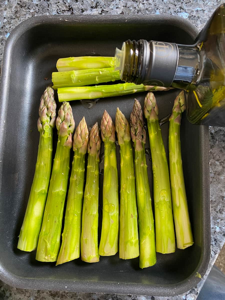 pouring olive oil over thick asparagus spears 