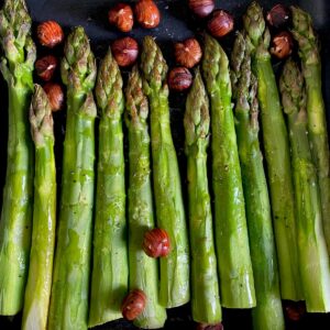 green asparagus spears baked in a roasting tin topped with toasted hazelnuts