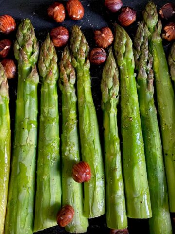 green asparagus spears baked in a roasting tin topped with toasted hazelnuts