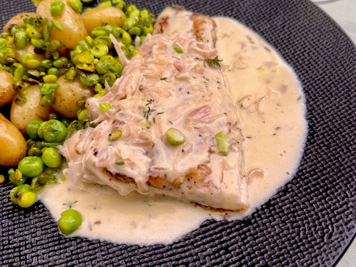 large fillet of sea bass fish served covered with a French beurre blanc sauce with the shallots showing