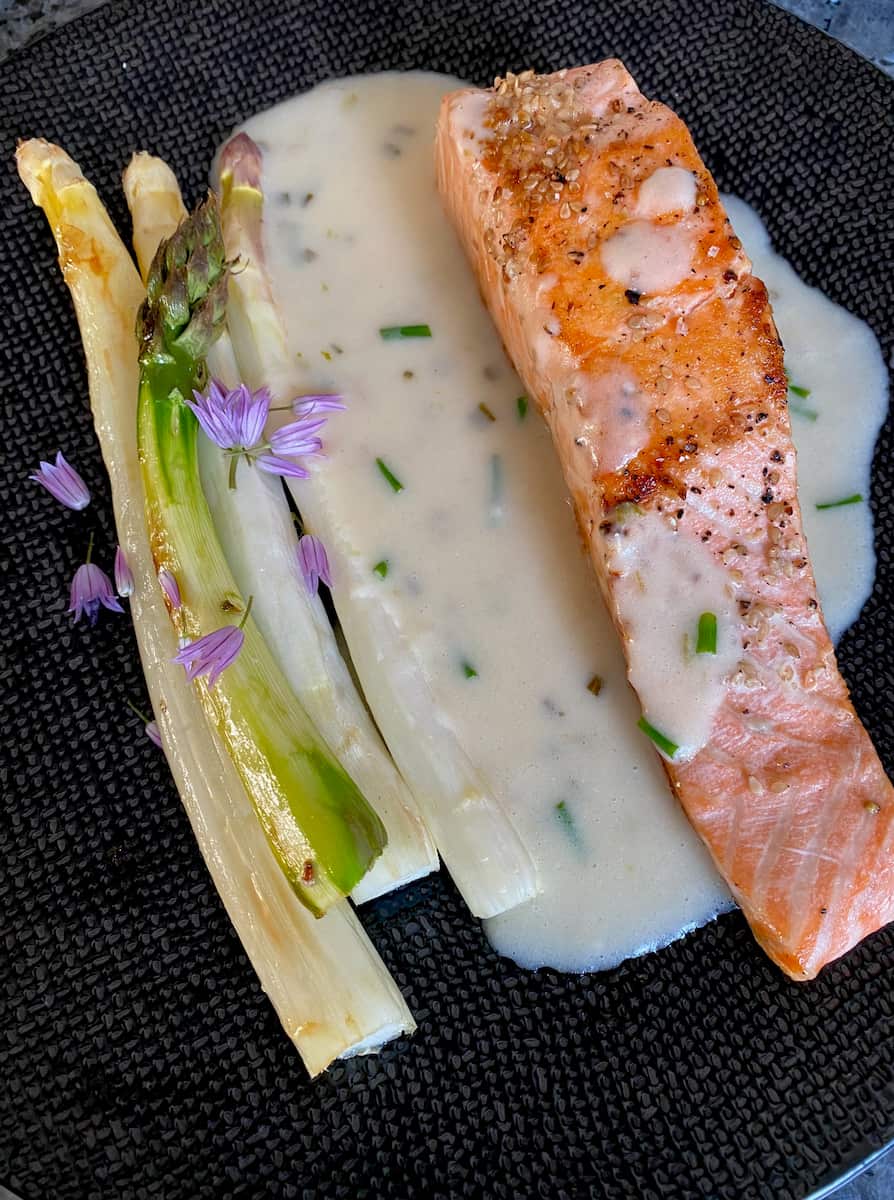 plate of pink salmon with asparagus spears, sauce, herbs and purple chive flowers